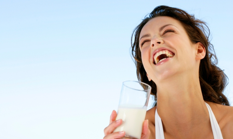 Donna sorridente con un bicchiere di latte, per illustrare probiotici per l’intolleranza al lattosio