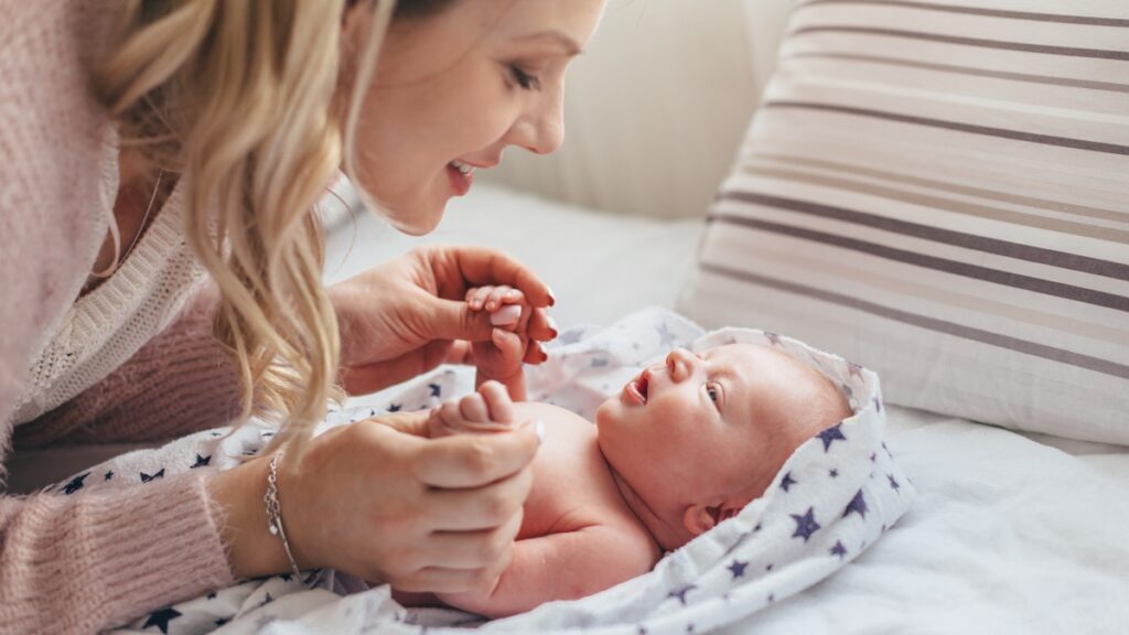 Madre che sorride al neonato sdraiato sul fasciatoio, per illustrare probiotici in gravidanza e coliche del neonato