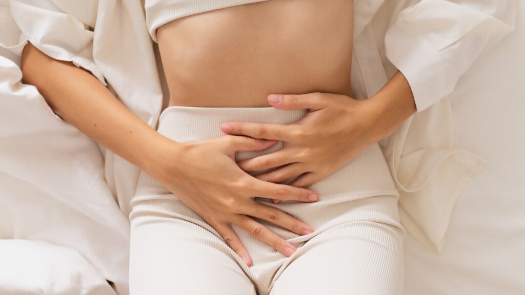 Donna sdraiata con le mani sul basso ventre, per illustrare microbiota vaginale e disturbi uroginecologici non infettivi