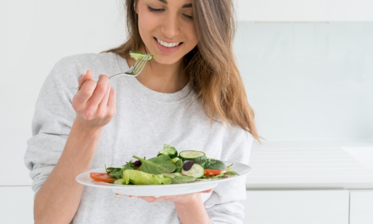 Donna sorridente mentre consuma un pasto ricco di verdure, per illustrare dieta e microbiota vaginale